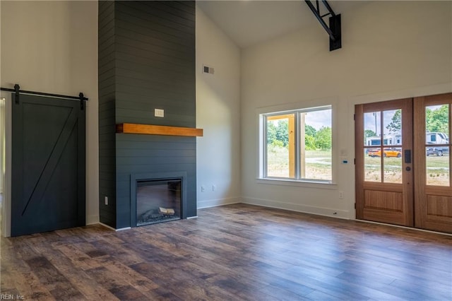 unfurnished living room featuring high vaulted ceiling, a barn door, a large fireplace, and dark hardwood / wood-style floors