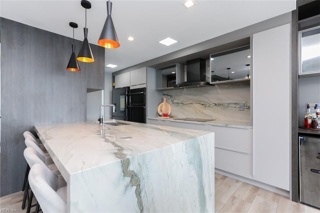 kitchen with sink, pendant lighting, wall chimney range hood, light hardwood / wood-style flooring, and backsplash