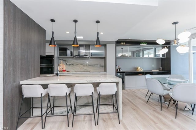 kitchen featuring light stone counters, pendant lighting, light wood-type flooring, and wall chimney exhaust hood