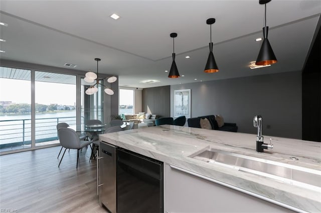 kitchen with a water view, light hardwood / wood-style floors, decorative light fixtures, and light stone counters