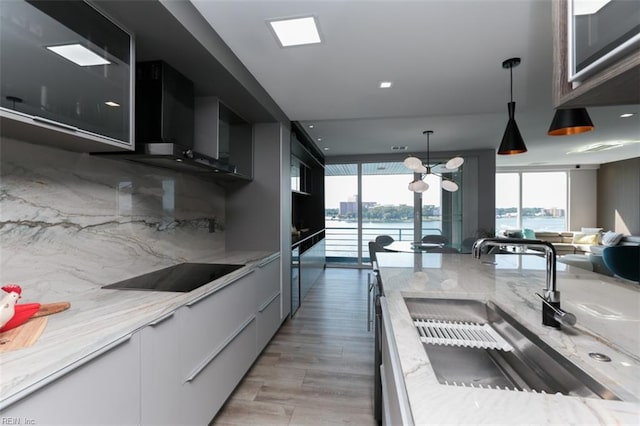 kitchen featuring a water view, light stone counters, tasteful backsplash, light hardwood / wood-style floors, and black electric stovetop