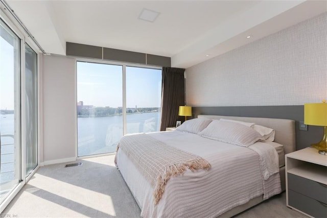 bedroom featuring light carpet, multiple windows, access to exterior, and a water view