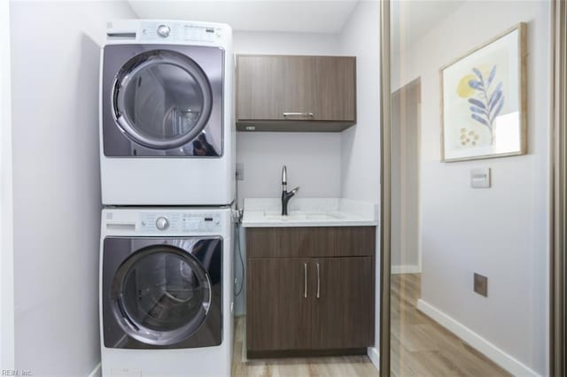 clothes washing area with cabinets, light wood-type flooring, sink, and stacked washer / drying machine