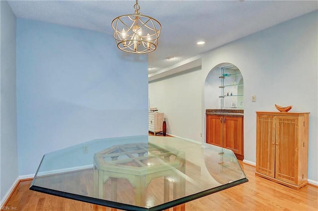 dining space featuring light wood-type flooring, an inviting chandelier, and a textured ceiling