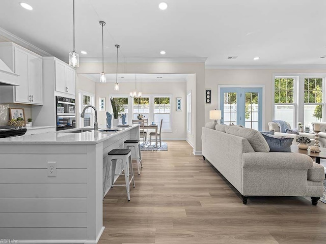 kitchen featuring light hardwood / wood-style floors, pendant lighting, crown molding, a notable chandelier, and white cabinetry