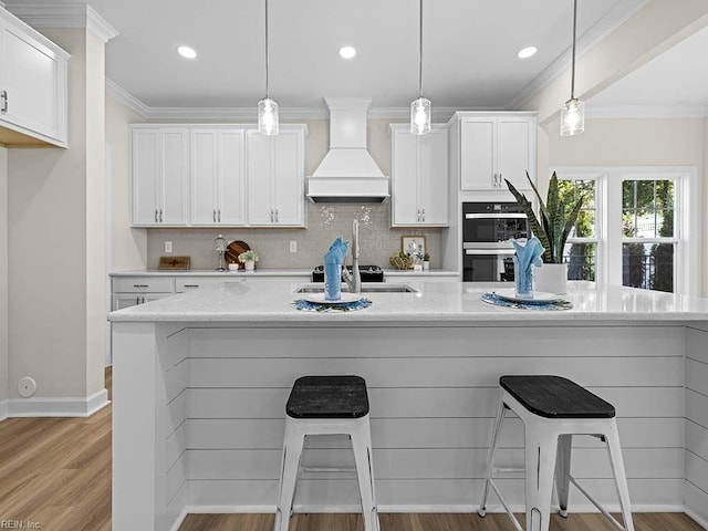 kitchen featuring light wood-type flooring, pendant lighting, custom exhaust hood, double oven, and white cabinetry