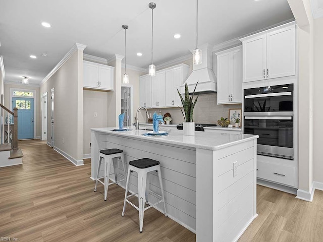 kitchen with a kitchen island with sink, light hardwood / wood-style flooring, backsplash, double oven, and white cabinetry