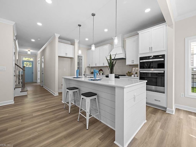 kitchen featuring white cabinets, an island with sink, plenty of natural light, and custom range hood