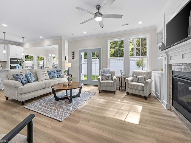 living room with ornamental molding, a fireplace, ceiling fan with notable chandelier, and light hardwood / wood-style flooring