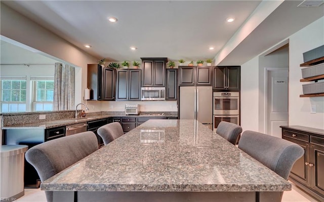 kitchen with a breakfast bar area, a large island, appliances with stainless steel finishes, and light stone counters