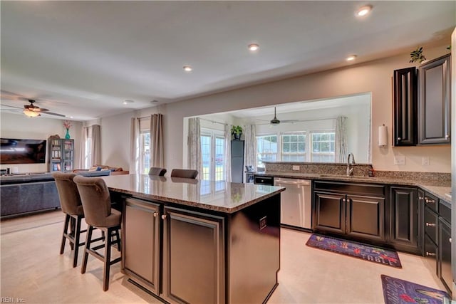 kitchen featuring a kitchen island, light stone counters, stainless steel dishwasher, sink, and a breakfast bar area