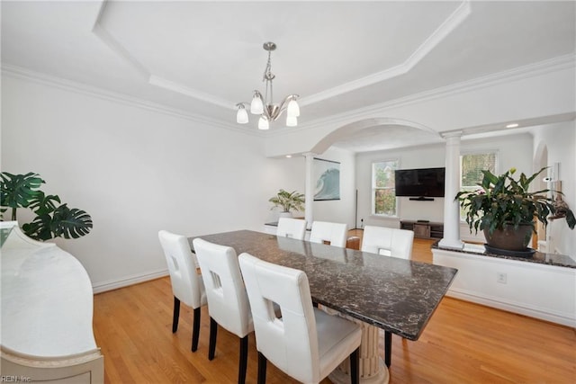 dining area featuring a raised ceiling, crown molding, an inviting chandelier, light hardwood / wood-style flooring, and decorative columns