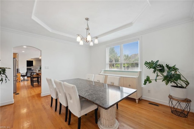 dining room with light wood-type flooring, crown molding, a chandelier, and a raised ceiling