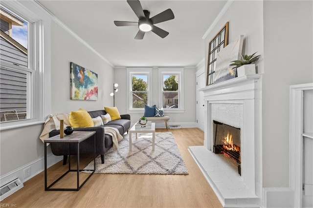 living room featuring a brick fireplace, crown molding, ceiling fan, and light hardwood / wood-style flooring