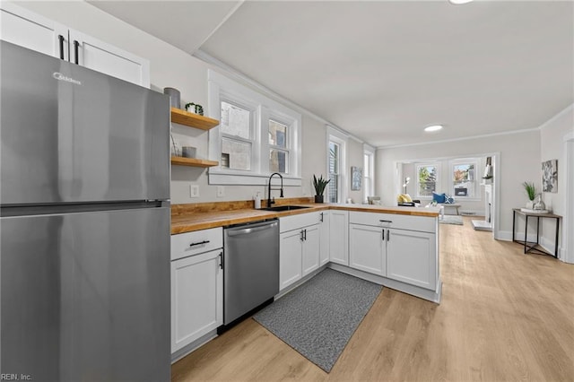 kitchen with appliances with stainless steel finishes, sink, white cabinetry, and wood counters