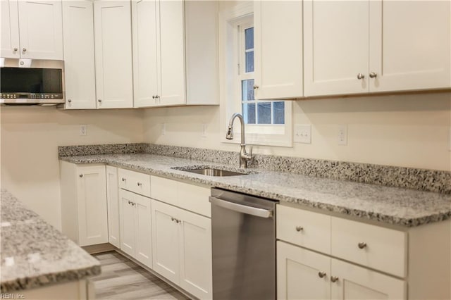 kitchen featuring light stone countertops, sink, stainless steel appliances, white cabinets, and light wood-type flooring