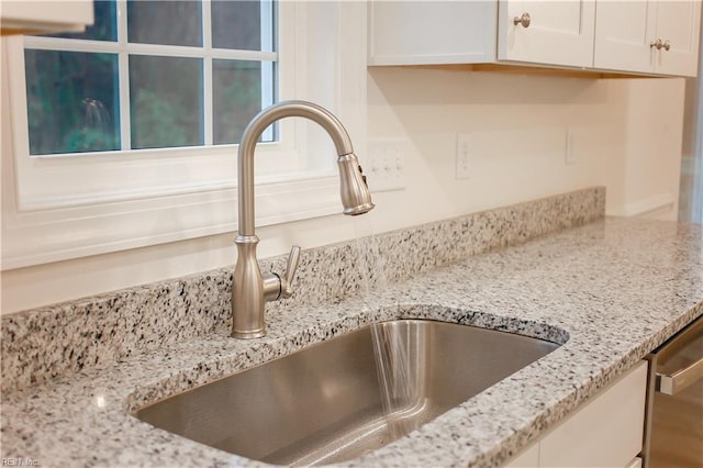 details featuring dishwasher, white cabinetry, light stone countertops, and sink