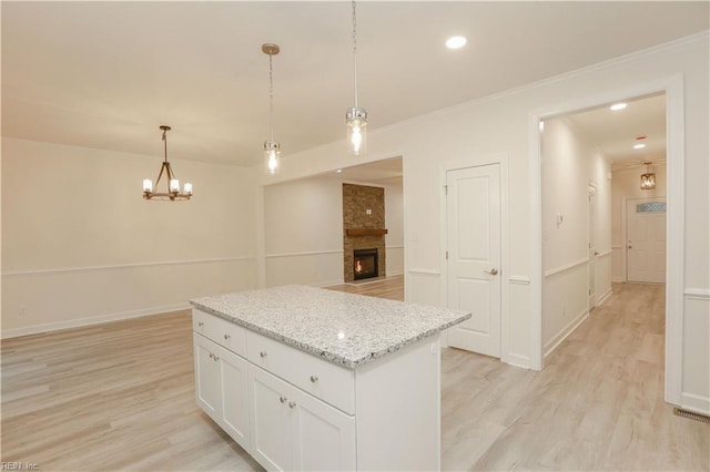 kitchen featuring white cabinetry, hanging light fixtures, light stone counters, a fireplace, and a kitchen island