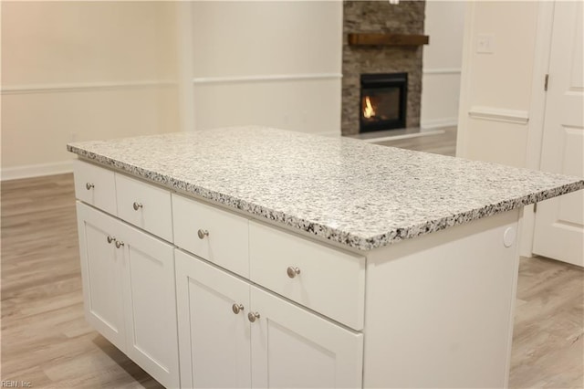 kitchen featuring a stone fireplace, white cabinetry, a center island, and light hardwood / wood-style floors