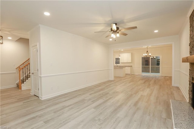 unfurnished living room with ceiling fan with notable chandelier, light hardwood / wood-style floors, a stone fireplace, and crown molding