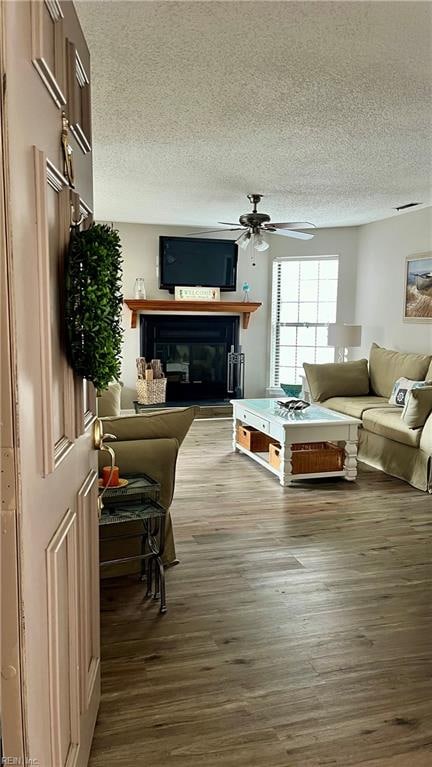 living room featuring wood-type flooring, a textured ceiling, and ceiling fan