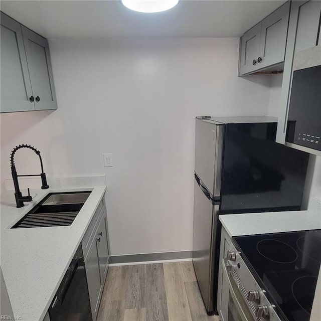 kitchen with gray cabinets, black dishwasher, sink, and light hardwood / wood-style flooring