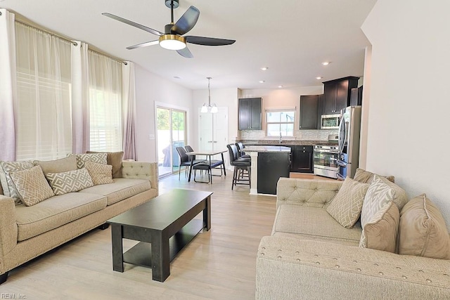 living room with ceiling fan with notable chandelier, light wood-type flooring, and sink