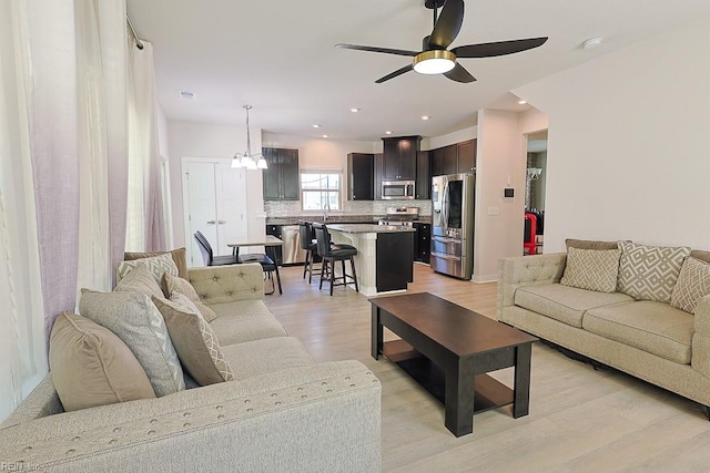 living room featuring ceiling fan with notable chandelier and light wood-type flooring