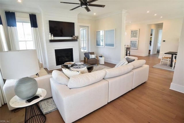 living room with ceiling fan, ornamental molding, a fireplace, and light hardwood / wood-style floors