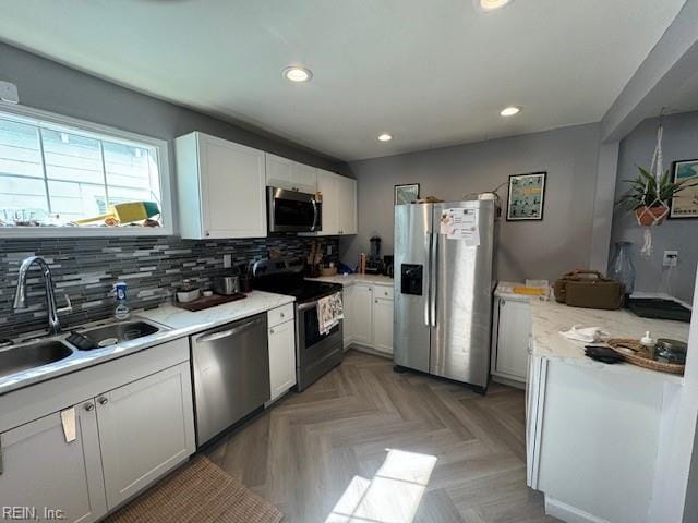 kitchen with white cabinets, light parquet floors, sink, appliances with stainless steel finishes, and backsplash