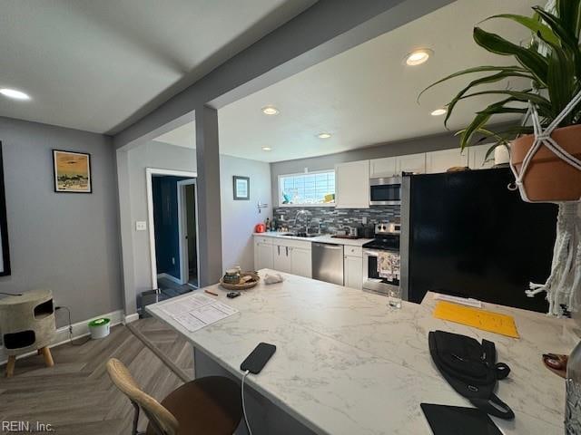 kitchen featuring sink, dark parquet flooring, light stone countertops, appliances with stainless steel finishes, and white cabinetry