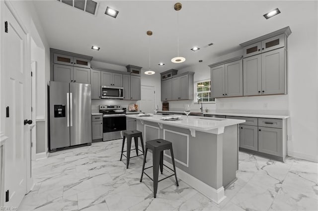 kitchen featuring pendant lighting, a kitchen island with sink, gray cabinets, appliances with stainless steel finishes, and a kitchen bar