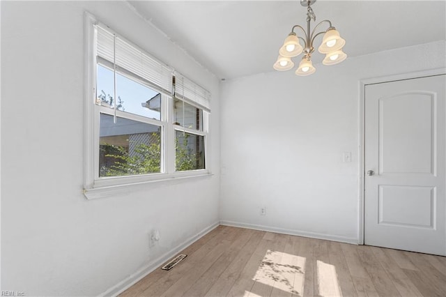 unfurnished room featuring a chandelier and light wood-type flooring