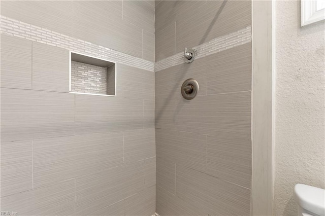 bathroom with a tile shower and toilet