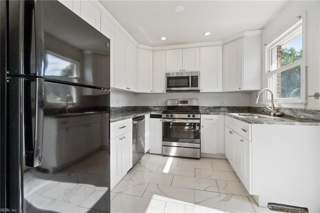 kitchen with dark stone countertops, sink, ornamental molding, white cabinetry, and appliances with stainless steel finishes