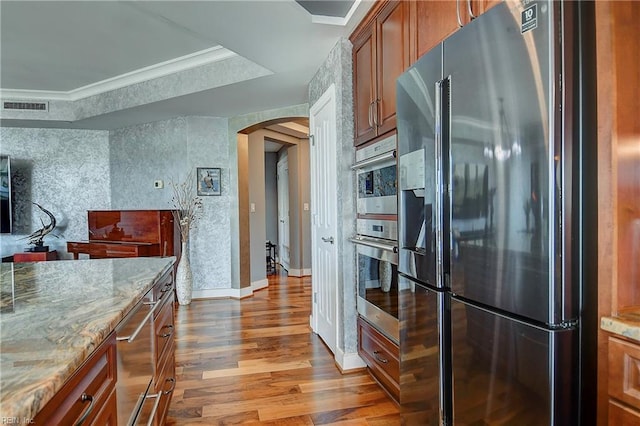 kitchen with stainless steel fridge, a tray ceiling, light hardwood / wood-style flooring, light stone counters, and ornamental molding