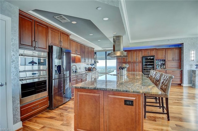 kitchen with light stone counters, exhaust hood, stainless steel appliances, a center island, and light wood-type flooring