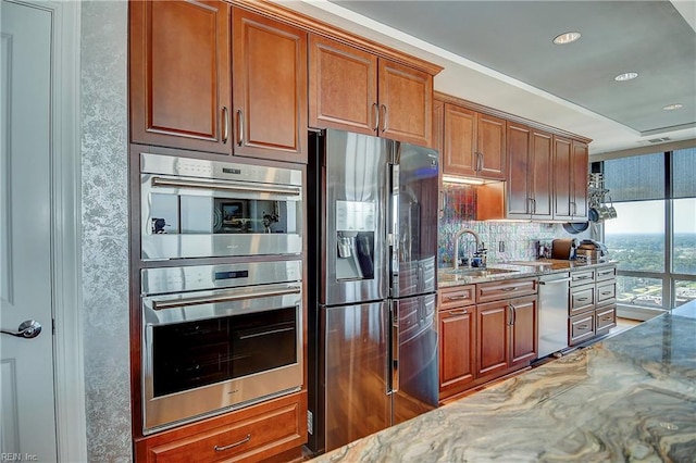 kitchen with tasteful backsplash, light stone counters, brown cabinets, appliances with stainless steel finishes, and a sink