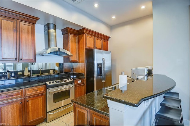 kitchen featuring dark stone counters, light tile patterned floors, wall chimney range hood, appliances with stainless steel finishes, and a sink