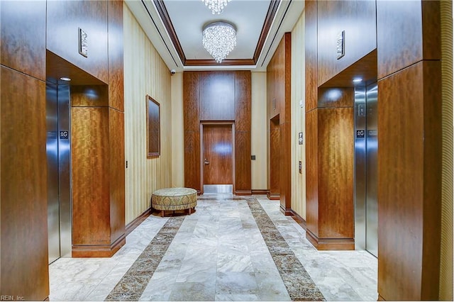 corridor featuring ornamental molding, a notable chandelier, wooden walls, and a towering ceiling