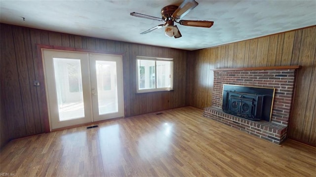 unfurnished living room featuring french doors, ceiling fan, wood walls, and light wood-type flooring