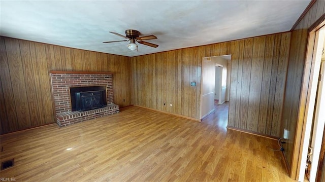 unfurnished living room featuring wooden walls, a brick fireplace, light wood-type flooring, and ceiling fan