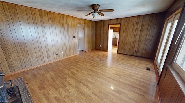 unfurnished room with light hardwood / wood-style floors, wood walls, plenty of natural light, and ceiling fan