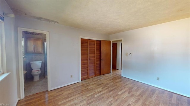 unfurnished bedroom featuring tile walls, light hardwood / wood-style flooring, a closet, and ensuite bathroom