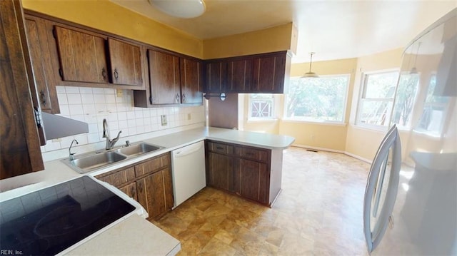 kitchen with kitchen peninsula, backsplash, pendant lighting, sink, and white appliances