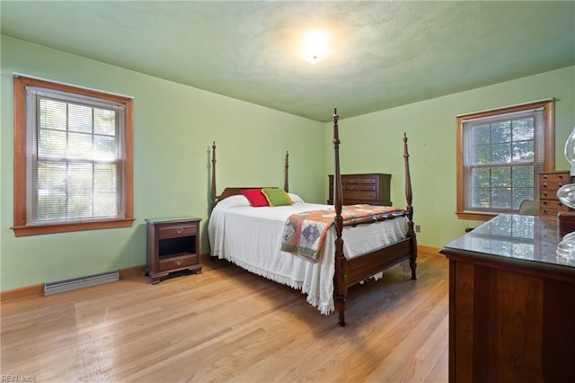 bedroom with light hardwood / wood-style floors and a baseboard heating unit