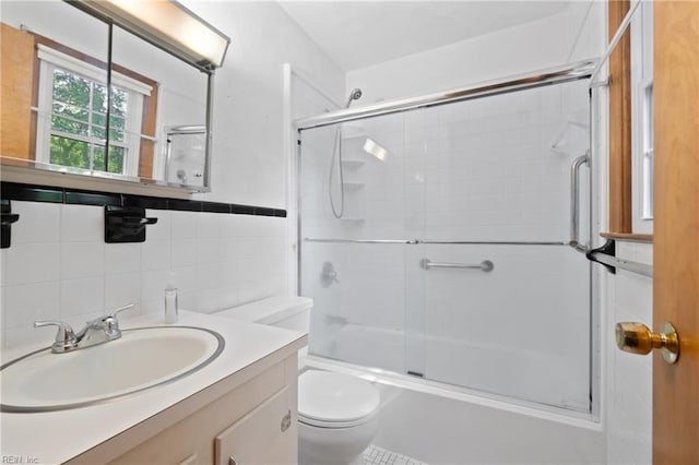 full bathroom with tile walls, combined bath / shower with glass door, vanity, and toilet