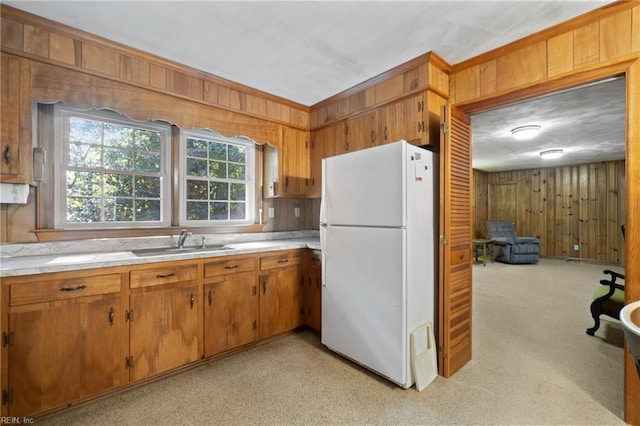 kitchen featuring light carpet, white refrigerator, wooden walls, and sink