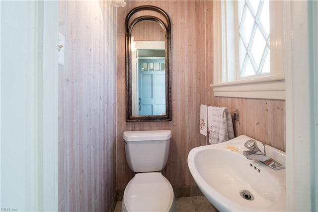 bathroom featuring toilet, wood walls, and sink