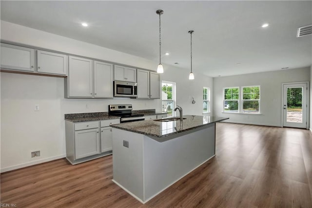 kitchen featuring dark stone countertops, wood finished floors, a sink, appliances with stainless steel finishes, and visible vents